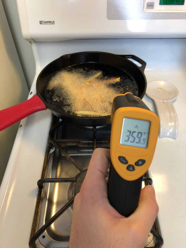 infrared thermometer being used on cast iron skillet with french fries