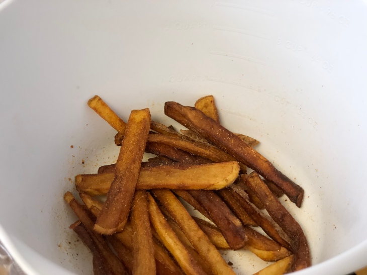 cooked french fries tossed in spices inside white bowl