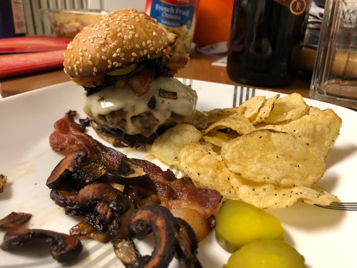 burger on plate with chips and pickles and extra mushrooms and bacon